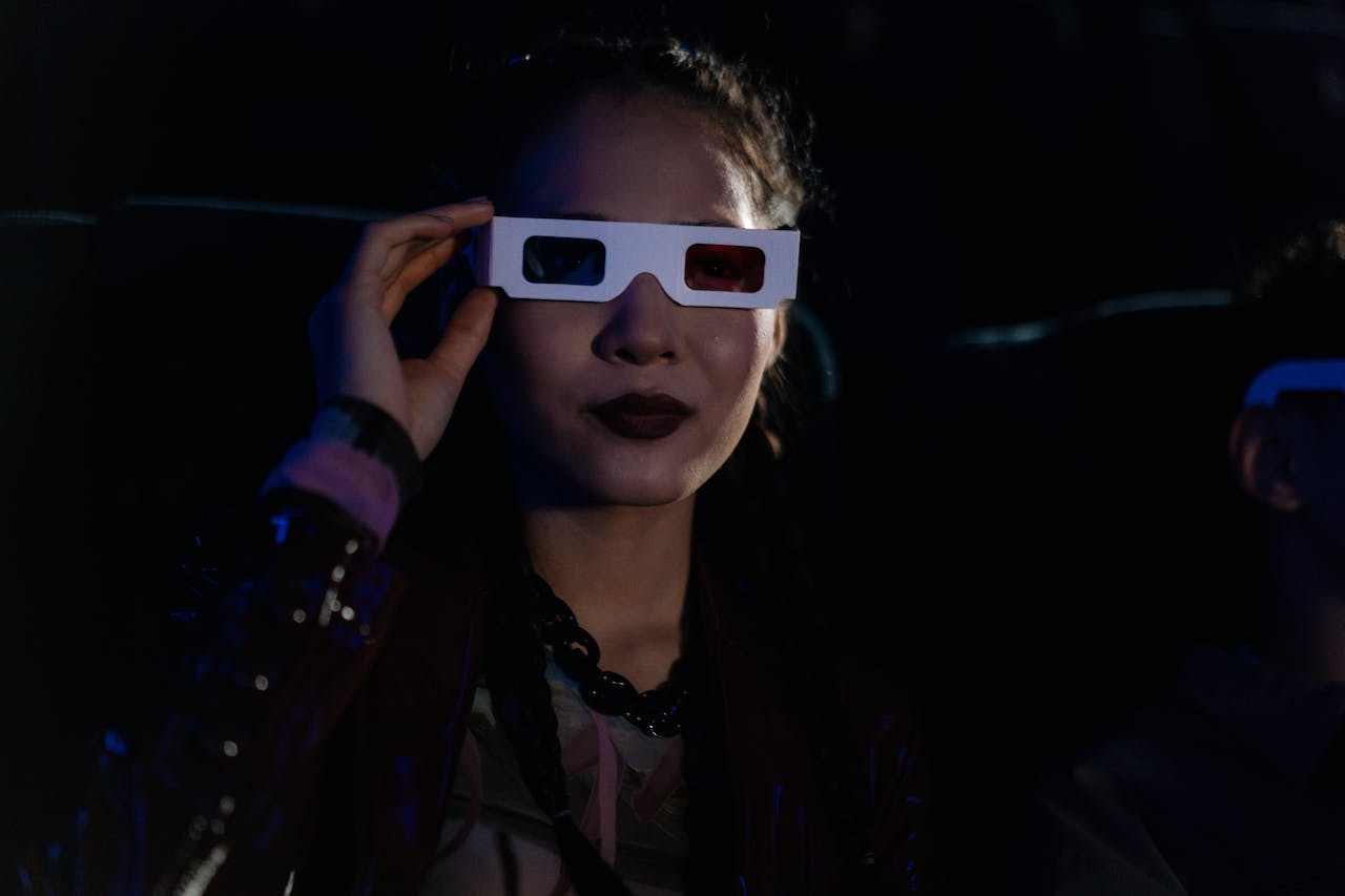 Kuvassa näkyy tyttö, joka katselee elokuvaa 3D-lasit päässään. Hänen kasvoillaan on ihastuksen ja keskittymisen ilme, kun hän uppoutuu virtuaalitodellisuuden maailmaan
