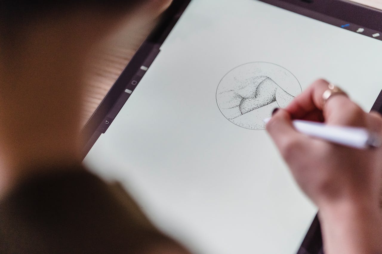 Kuvassa näkyy nainen piirtämässä piirtolevylle tabletilla. Hänen luovuutensa kukoistaa digitaalisessa taiteessa